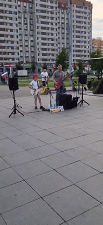 Father-son guitar duo performs street music outside apartment building