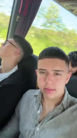 The video shows two young men riding in a bus, likely on a highway. The man closest to the camera is wearing a gray linen shirt, the other is wearing a white t-shirt under a black zip up jacket and glasses. He appears to be sleeping, head leaning on the bus window. Fast paced music is playing.