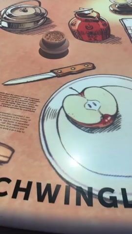 The camera pans over a cartoon drawing of a table with various food items. The drawings are made in a black and white, pen and ink style. The table appears to be covered with a peach-colored cloth. There is a cut apple on a plate, a knife, a small pot of spices, a teapot, a jar of jam, three apples on a checkered cloth, a mug of purple liquid, and a blurred gray object.