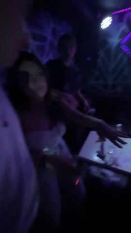 The video shows a dimly lit nightclub with blue lights. People are dancing, and some are standing around tables. The camera moves erratically, making it difficult to see details clearly. A decorative wall with diamond-shaped lights is visible.