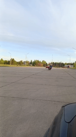 Teen rides red motorcycle in empty Russian parking lot