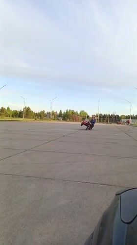 Teen rides red motorcycle in empty Russian parking lot