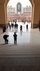 Large crowd gathers in Tehran plaza, viewed through marble archway
