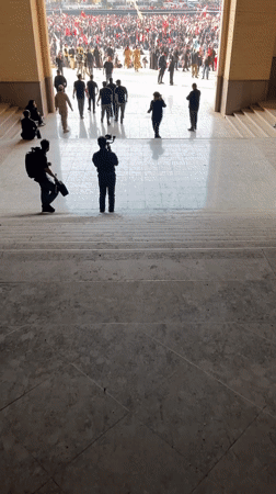Large crowd gathers in Tehran plaza, viewed through marble archway