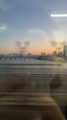 Train passenger films Seoul cityscape under colorful evening sky
