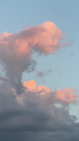 The video shows a close-up view of a sky filled with clouds. The clouds are a mix of gray and pink hues, suggesting a sunset or sunrise. The sky itself is a pale blue. There are no people or objects visible in the frame. The focus is entirely on the atmospheric conditions and the soft colors of the clouds.