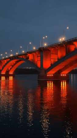 Red-lit Kommunalny Bridge captured across Krasnoyarsk at dusk