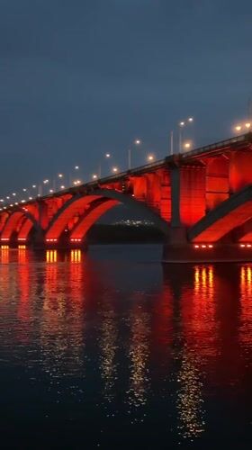 Red-lit Kommunalny Bridge captured across Krasnoyarsk at dusk