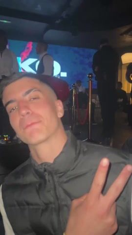 A video shows a man making a peace sign at a nightclub. The camera then pans back to show two DJs working a Pioneer board, surrounded by other people. There are two large, red, oval speakers behind the DJ booth.