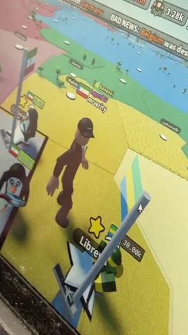 The image displays a close-up of a computer screen showing a video game. The game appears to be a world-building or strategy game, with a colorful, stylized map.

**Subjects:**
*   **People:** A 3D avatar of a person in a black suit and cap is prominently featured in the foreground. There are also two stylized penguin characters with flags on stands in the left middle ground.
*   **Objects:** The game features flags of various countries, stands with flags, buildings represented by simple shapes, trees, and an airplane icon.
*   **Scene:** The scene is a digital representation of a world map divided into colored territories. The foreground shows a detailed section of the map with interactive elements.
*   **Setting:** The game's setting is a virtual world map. The context provided is Torquay, United Kingdom, though this information is external to the image itself and not directly depicted.

**Activity or Event:**
The game appears to be in progress, with player avatars and game elements interacting on the map. The presence of population counts and country names suggests a simulation or management aspect to the gameplay. The "BAD NEWS: Belgium was destroyed" text indicates a potential conflict or event within the game.

**Notable Details:**
*   **Time of Day/Weather:** Not discernible from the image. The game environment is brightly lit and colorful.
*   **Location Cues:** Text labels within the game indicate places like "Libreville," "Gabon," "Makokou," and "[Banana] Legend IV mrverity." The flags visible include those of Italy and Gabon.
*   **Emotions:** No emotions are conveyed as the subjects are digital avatars or stylized characters.

**Visible Text:**
*   "BAD NEWS: Belgium was destroyed and forced to accept France's Peace"
*   "Torquay" (appears to be a label for a location within the game map, though the provided context suggests this is the external location of the recording)
*   "Bertoua"
*   "Makokou"
*   "[Banana] Legend IV mrverity"
*   "Libreville"
*   "Gabon"
*   "Population: 509.59k"
*   Numerical values like "30.00K", "30.00K", "41.520", "95.66m" are also visible, likely representing currency, population, or other game statistics.
*   A game ID "XOBJB2D" is visible.