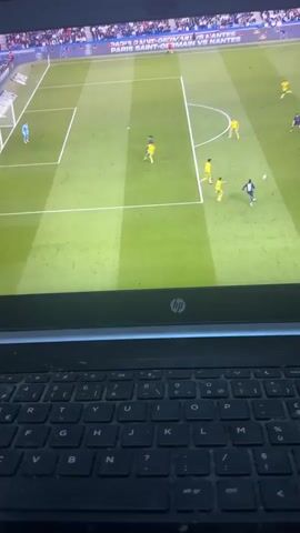 The image shows an HP laptop with a football match playing on its screen. The screen displays a green football pitch with white lines, a goal, and several football players. One team wears yellow kits, and the other wears dark blue/black kits. A goalkeeper in a light blue kit is positioned near the goal. On the screen, one player in a dark kit is close to the goal with the ball, while other players from both teams are in the vicinity, suggesting an active play or a potential scoring opportunity. Visible text on the screen includes "PARIS SAINT-GERMAIN VS NANTES" and "MERCREDI 27 MAI". The black keyboard of the laptop is visible in the foreground. The activity taking place is watching a football match indoors. The provided location context is Saint-Leu-d'Esserent, France.
