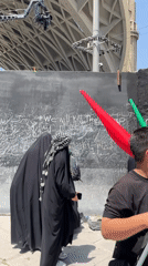 Group pauses at graffiti-covered black wall in Tehran