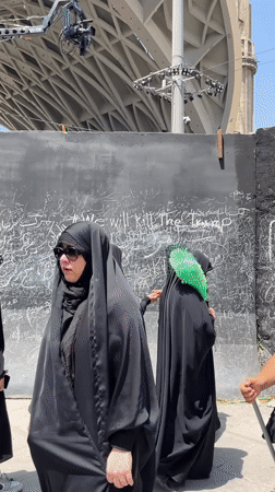 Group pauses at graffiti-covered black wall in Tehran