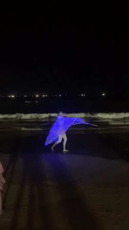 Blue-lit wing costume spins on a Đà Nẵng beach at night