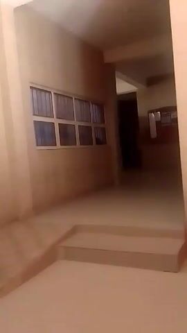 The camera travels through an interior hallway with beige walls. There's a ramp and steps leading to another section of the hall. A window with multiple panes is visible to the left. As the camera pans, a scooter appears briefly, and then the focus shifts to a large poster. The poster is positioned beside a doorway, and there's a sign above it that reads "DEPARTMENT OF RADIOGRAPHY AND RADIATION SCIENCES".  The poster's design includes a symbol often associated with radiation. The hallway appears to be in a building or facility related to radiography or radiation sciences.