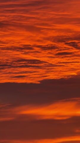 The video shows a vibrant sunset with orange and red hues filling the sky. The clouds are layered, creating a textured effect. A street light briefly appears in the frame, followed by a road sign indicating directions to "Chester A548" and "Birkenhead A552."