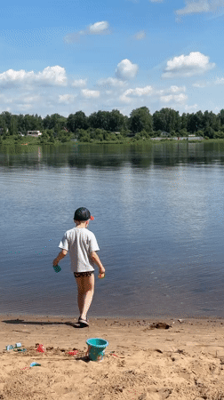 Boy stands on sandy shore overlooking water in Yaroslavl