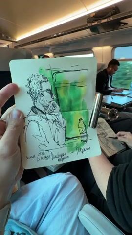 The video shows a first-person perspective of someone holding a sketchbook on a train. The sketchbook contains a sketch of a man with curly hair and glasses, rendered in black ink with some green watercolor accents. Below the sketch, there is handwritten text in what appears to be Cyrillic. In the background, other passengers are visible on the train, some of whom are also engaged in creative activities like drawing. The train interior features seats, a table, and windows through which the passing scenery can be glimpsed. The lighting suggests it is daytime.