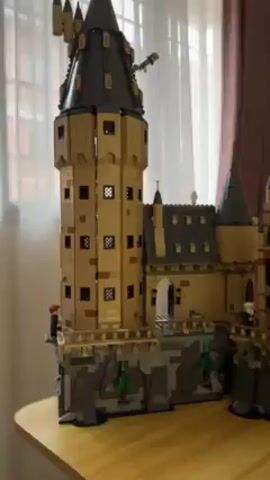 Here's a concise description of the video:

The video shows a large Lego replica of Hogwarts School of Witchcraft and Wizardry from the Harry Potter series. The model is intricately detailed, featuring towers, turrets, windows, and other architectural elements. The model sits on a wooden table in a room with a window covered by sheer curtains.  An air conditioning unit is visible on the wall. A woman appears briefly at the edge of the frame. The camera pans across the model, showcasing its scale and complexity.