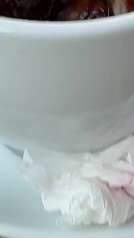 The video shows a close-up view of a dark red, viscous substance, possibly food, with glistening surfaces. A metallic object, possibly a spoon or spatula, is partially visible within the substance. The substance appears to be in a container or on a surface with a light-colored background.