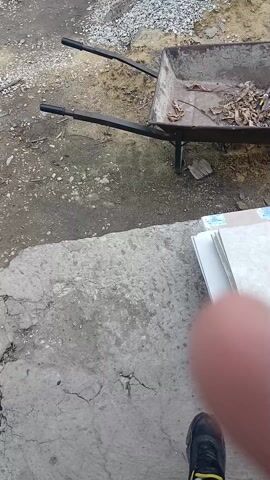 The video shows a partial view of a concrete surface, a wheelbarrow containing leaves and debris, a pile of tiles, and a finger in the foreground. The area surrounding the concrete surface appears to be dirt or gravel. The wheelbarrow has black handles and a metal basin. The tiles are white or light-colored. The finger is out of focus.