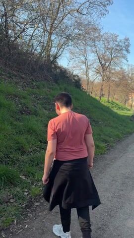 A young person walks along a path, turns, and points off the path toward a grassy hill. The camera follows the direction of the person's point, and focuses on a white rabbit with black spots. The rabbit is near some dead tree branches in the grass.