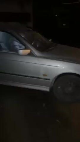 The video shows a silver sedan parked outside at night. The car is facing left and the front right tire is visible. The camera pans across the side of the car and then to the front, revealing the car’s license plate number: CT 4044 PT. A building is visible in the background.