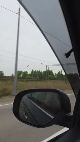The video is shot from the dashboard of a moving vehicle driving down an empty road at twilight.  Streetlights line the road, and parallel to it on the left side are train tracks.  A sparse line of trees can be seen in the distance where the sun is setting.