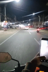 Scooter rider uses phone while driving through Lhokseumawe street