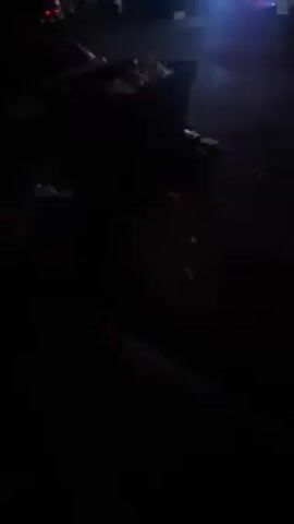 The video shows a dark, seemingly outdoor area. There's litter scattered on the ground. A vehicle is partially visible at the edge of the frame. A loud noise, possibly a vehicle engine, is heard.