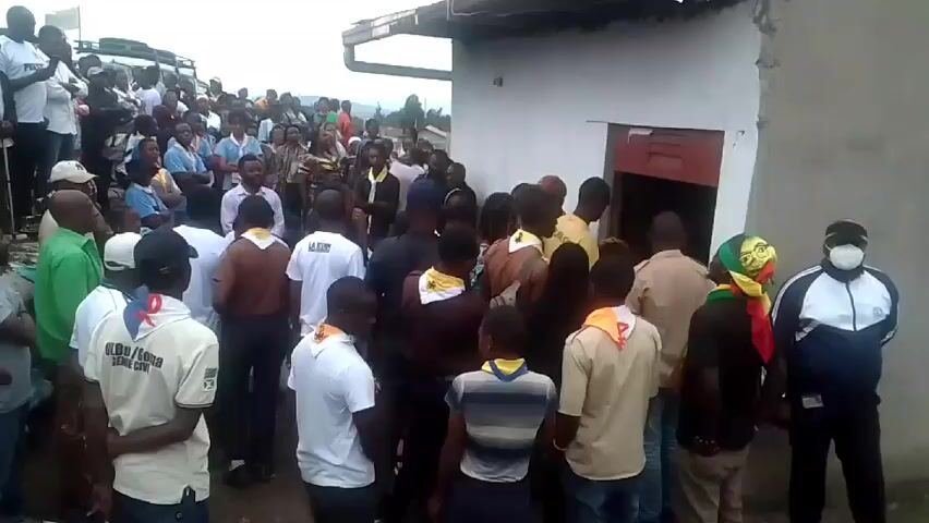 Here is a description of the video:

The video shows a large group of people gathered outside a small, white building. Many people are wearing scout uniforms. Some people are standing on a vehicle to get a better view. The crowd is fairly dense around the building. There appears to be a ceremony or gathering taking place.