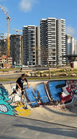 Young person rides scooter at graffiti-covered skate park in Bat Yam
