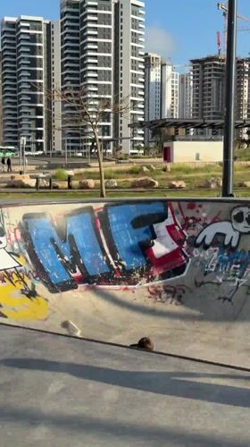 Young person rides scooter at graffiti-covered skate park in Bat Yam