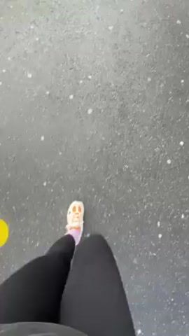 The video shows a first-person view of someone walking on a paved surface, then panning up to reveal a parking area with a mountain backdrop. The mountain is partially covered in trees and has visible rock faces.  The parking area is marked with yellow lines and signage. A crosswalk with yellow stripes leads to a large, dark wooden building. The weather appears cloudy.