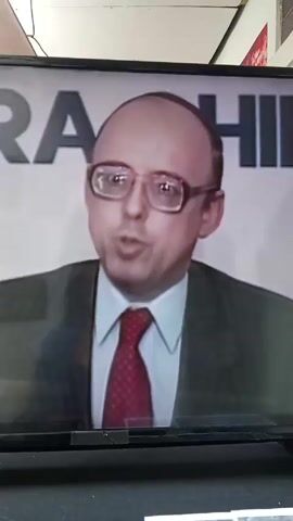 A TV screen shows a man sitting on a chair. He is wearing a suit and glasses. Behind him is a sign that says "Jaime Parra Hilma". Animated images of a shark, a lion, a pencil, a fly, and a cat on a stool appear around him. Children with white gloves on their hands are visible at the bottom of the screen.