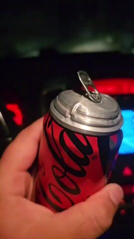 A hand holds a crushed can of Coca-Cola Zero in front of a dark background with blurred red and blue lights. The can is red and black with a white Coca-Cola logo. The pull tab is open, and the can appears to be dented. The video is short, with no discernible action beyond holding the can.