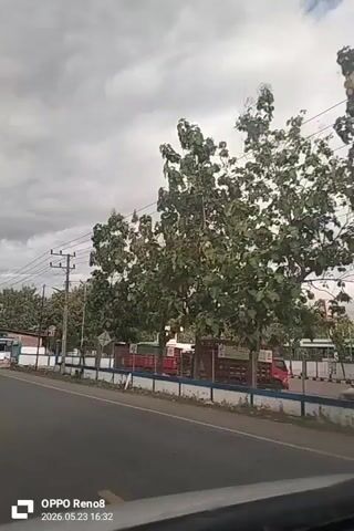 The video shows a view from a car driving on a road, with a red truck ahead in the same lane. The truck has "PT. CITRA HOE SABEE" written on its side. A motorcycle is seen passing the truck on the left. The sky is overcast and cloudy. Power lines run along the side of the road. Trees and buildings are visible in the background. The video is recorded with an OPPO Reno8 phone and has a timestamp of 2026.05.23 16:32.