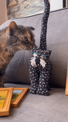 Cat plays with paintings and toy doll on sofa