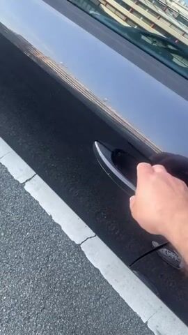 The video begins with a close-up of a hand opening a dark-colored car door. The car appears to be an Audi, indicated by the logo visible on the steering wheel in later shots. The scene is outdoors, with asphalt and a white line visible on the ground, suggesting the car is parked by a road or in a parking lot. The weather appears to be fair, with daylight suggesting it is daytime.

The camera then moves inside the car, showing the driver's seat, dashboard, and steering wheel. A foot wearing a grey and white sneaker enters the frame and moves towards the pedals. The driver's leg, clad in denim shorts, is also visible. The interior of the car is modern and sleek, typical of an Audi.

The video continues with a shot of the steering wheel, clearly showing the Audi rings emblem. The perspective shifts again, looking towards the dashboard and steering column. The activity depicted is someone entering a car and preparing to drive. The overall tone is casual and everyday. There is no visible text in the video. The location context of Wuppertal, Germany, does not provide any specific visual cues within the video itself.