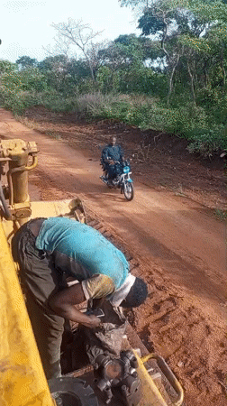 Construction worker maintains heavy machinery on Nigeria dirt road