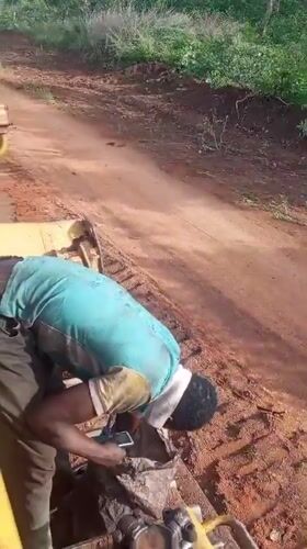 Construction worker maintains heavy machinery on Nigeria dirt road