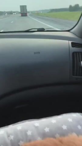 A close-up video shows a ginger cat curled up in a car. The cat is on a grey cushion with white stars. The car's dashboard, including an air vent, is visible in the background. The video is shot from a high angle looking down at the cat.