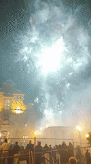 Fireworks and procession mark a nighttime religious festival in a town square.