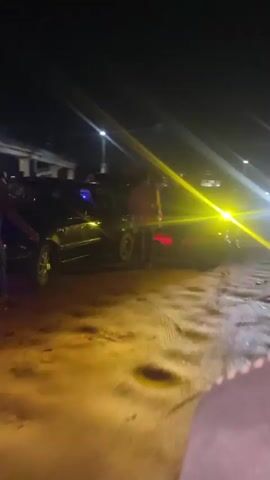 The video captures a nighttime scene in Sauka, Nigeria, filled with activity. The primary subjects are people and various vehicles, including motorcycles, cars, and what appears to be a bus and a pickup truck. The setting is an outdoor area, likely a street or a busy hub, illuminated by artificial lights from streetlamps and vehicle headlights.

The activity taking place is a bustling gathering, with people moving around and interacting with the vehicles. The presence of multiple vehicles and people suggests a lively atmosphere, possibly a market, a social event, or a transportation hub operating late into the night. The lighting is stark, with bright beams from headlights cutting through the darkness, creating strong contrasts and lens flares.

Notable details include the time of day, clearly nighttime, with a dark sky. The weather appears to be clear, as there are no visible signs of rain or fog. The location cues are tied to Sauka, Nigeria, implying an urban or semi-urban environment. The overall emotion conveyed is one of energy and dynamism, despite the darkness. The video's focus is on movement and the interplay of light and shadow, highlighting the human and vehicular presence in the nocturnal landscape. There is no visible text in the video.
