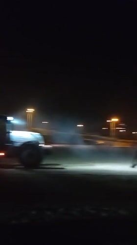 Tractors work Barcelona beach under city lights at night
