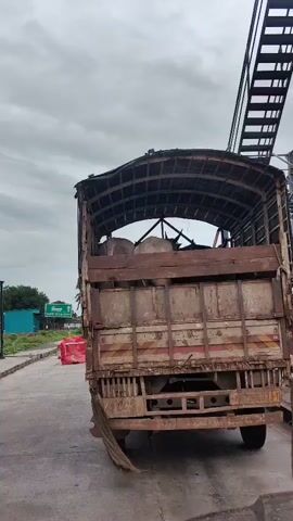 THE VIDEO SHOWS THE REAR VIEW OF A TRUCK CARRYING CATTLE. THE TRUCK IS RUSTY AND APPEARS TO BE OLD. THE CATTLE ARE PACKED CLOSE TOGETHER UNDER A TARP ROOF. THE SKY IS CLOUDY.