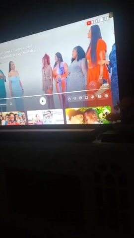 A person is watching the YouTube show "Hunt Game 2.1 Ladies Edition" on a television. The show features a man and five women standing in a line. The screen also shows thumbnails of other videos available to watch. The room the television is in is dark.