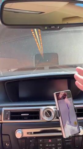 The video shows a view from the driver's seat of a car traveling through a brightly lit, long tunnel. The interior of the car is visible in the foreground, including the dashboard with a digital climate control display showing "21.5" and "22.0". A smartphone mounted on the dashboard displays a navigation app with a route marked in blue, indicating "45 KM" to "6725 - Dimokratias". The time on the phone is "17:31", and the date appears to be "10/10/2023". The tunnel walls are illuminated by a series of lights running along the ceiling, creating a tunnel effect. Another car is visible in the distance within the tunnel. The overall impression is of a journey through an urban or infrastructure passage. The yellow hue of the tunnel lights and the slight haziness suggest the environment within the tunnel. The car is moving forward, indicated by the changing perspective of the tunnel. There is no indication of weather or time of day beyond what is displayed on the phone, but the tunnel implies an enclosed and possibly underground or covered roadway. The scene is neutral and functional, focused on the act of travel.