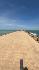 Cyclist rides concrete pier amid turquoise waters in Tangier
