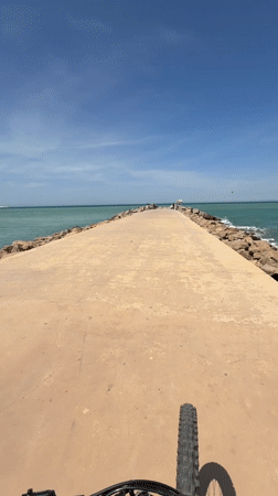 Cyclist rides concrete pier amid turquoise waters in Tangier